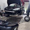 Mécanicien inspectant le bloc moteur avant le remplacement du kit de distribution complet sur un véhicule Peugeot démonté.