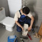 Plombier réparant le mécanisme de chasse d'eau à l'intérieur d'un réservoir de WC à Thonon-les-Bains.