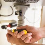 Plombier de chez Dépan’Services Gaz & Eau dépannage d'un raccord de siphon en plastique sous un évier.