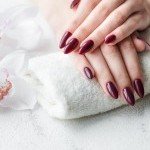 Pose de vernis bordeaux brillant sur ongles en gel de forme amande à l'institut de beauté XXL Coiffure Annemasse